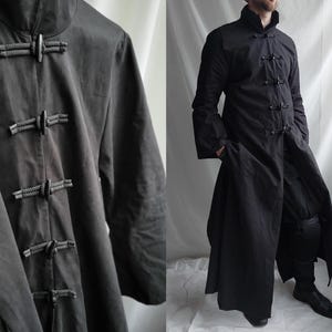 May include: Black long coat with a mandarin collar and decorative frog closures. The coat is floor-length and has long sleeves. The coat is shown on a person.