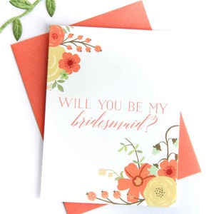 以下が含まれることがあります： オレンジと黄色の花柄が描かれた白いカード。"Will you be my bridesmaid?"というテキストがオレンジ色で書かれています。