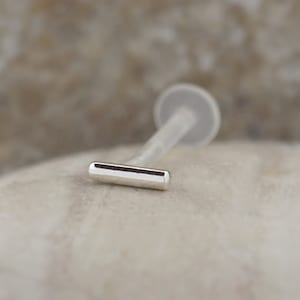 May include: A silver barbell with a straight bar, designed for body piercing.
