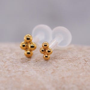 Op de afbeelding: Twee gouden lichaamssieraden met een cluster van kleine balletjes. De sieraden zijn op een witte achtergrond.