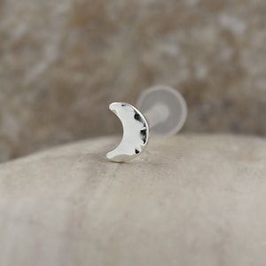 May include: A silver crescent moon stud earring. The moon is hammered and has a textured surface.