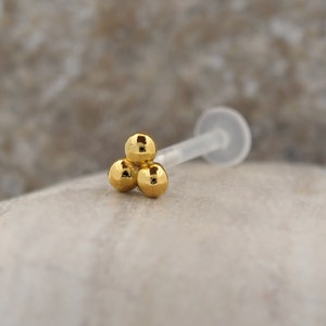 Peut inclure: Bague de nez en or avec trois boules et une tige en plastique transparente.