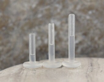 May include: Three clear plastic nose studs of different lengths. The studs are all the same diameter and have a flat base.