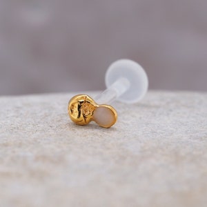 May include: A gold and white body jewelry piece with a clear plastic post. The jewelry is a small, round shape with a flat back.