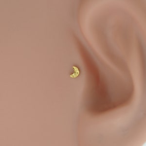 Puede incluir: Un piercing de nariz en forma de media luna de oro. El pendiente es peque&ntilde;o y delicado, con una superficie texturizada.