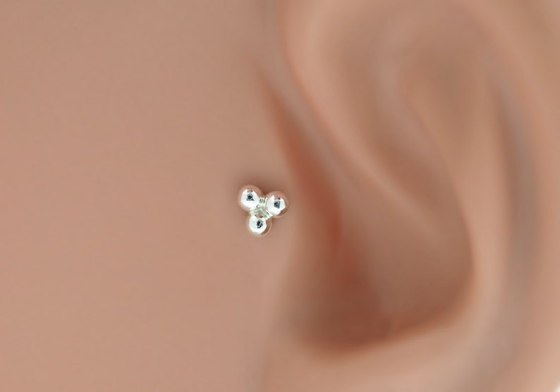 Peut inclure: Un clou de nez en argent avec trois petites boules rondes.