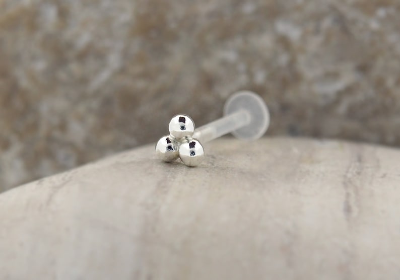 Peut inclure: Bague de nez en argent avec trois boules et une tige en plastique transparente.