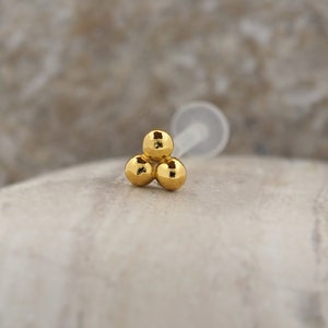 Peut inclure: Bague de nez en or avec trois boules. Le piercing de nez a trois petites boules dor&eacute;es.