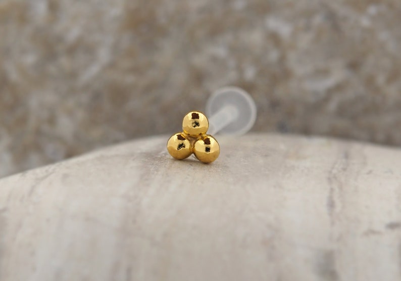 Peut inclure: Bague de nez en or avec trois boules. Le piercing de nez a trois petites boules dor&eacute;es.