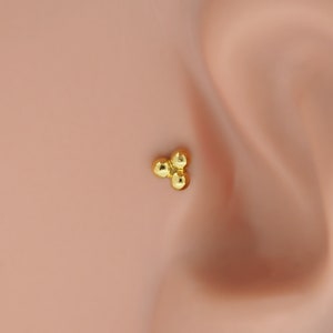 Peut inclure: Un piercing de nez en or avec trois petites perles rondes.