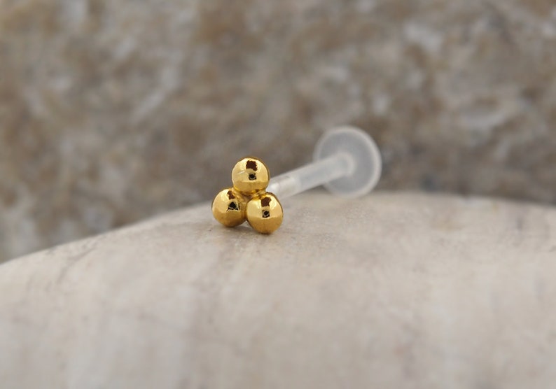 Peut inclure: Bague de nez en or avec trois boules et une tige en plastique transparente.