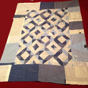 May include: A quilt made from repurposed blue and white patterned fabric. The quilt is made up of squares and triangles, and the fabric is sewn together in a geometric pattern.