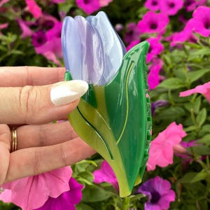 K&ouml;nnte beinhalten: Eine Haarspange in Form einer Tulpenbl&uuml;te mit durchscheinenden hellvioletten Bl&uuml;tenbl&auml;ttern und einer gl&auml;nzenden gr&uuml;nen Basis aus Stiel und Blatt. Das Accessoire hat eine glatte, polierte Oberfl&auml;che und einen funktionalen Federverschluss.