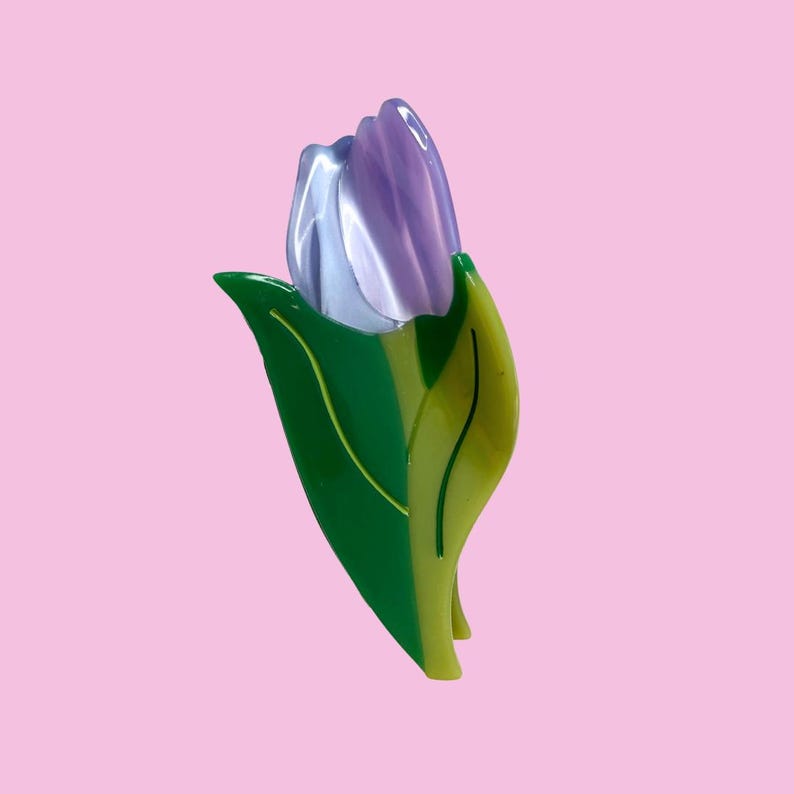 K&ouml;nnte beinhalten: Eine Haarspange in Form einer Tulpenbl&uuml;te. Der Bl&uuml;tenkopf ist aus gl&auml;nzendem, durchscheinendem Hellviolett gefertigt, w&auml;hrend der Stiel und die Bl&auml;tter aus massivem, leuchtend gr&uuml;nem und hellgr&uuml;nem Acryl mit eingravierten dunkelgr&uuml;nen Blattadern bestehen.