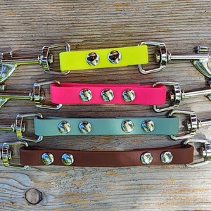 May include: Four dog leash coupler attachments with metal swivel clips. The couplers are made of rubber and come in yellow, pink, gray, and brown.