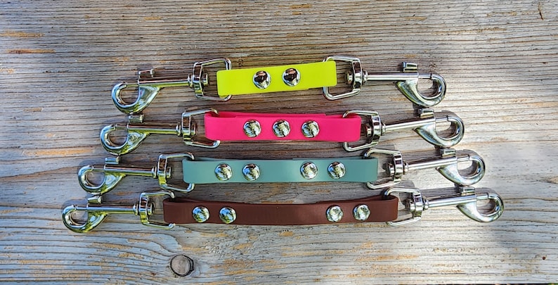 May include: Four dog leash coupler attachments with metal swivel clips. The couplers are made of rubber and come in yellow, pink, gray, and brown.