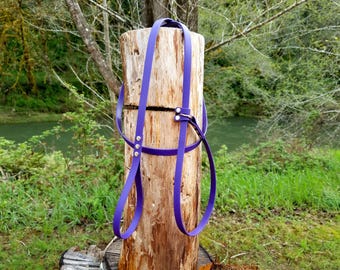 May include: A purple harness constructed from smooth, flexible material featuring adjustable straps, silver-toned metal rivets, and a central metal ring connector, designed with a continuous loop configuration for secure attachment.