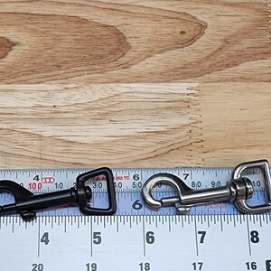 May include: Five metal swivel snap hooks in different finishes: silver, black, nickel, and gold. The hooks are lined up on a ruler with measurements in inches.
