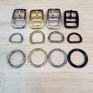May include: Assortment of metal buckles and D-rings in silver, gold, and black finishes. The buckles have two holes and the D-rings are various sizes.