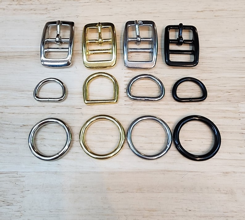 May include: Assortment of metal buckles and D-rings in silver, gold, and black finishes. The buckles have two holes and the D-rings are various sizes.