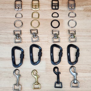 May include: Assortment of metal hardware, including buckles, rings, swivels, carabiners, and hooks in silver, gold, and black finishes.