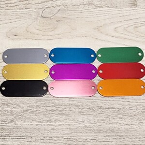 May include: Eight oval-shaped metal tags in different colours: silver, blue, green, gold, purple, red, pink, and orange. The tags have two holes on each side.