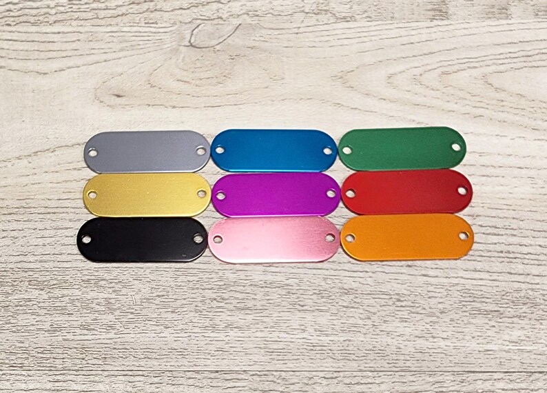 May include: Eight oval-shaped metal tags in different colours: silver, blue, green, gold, purple, red, pink, and orange. The tags have two holes on each side.