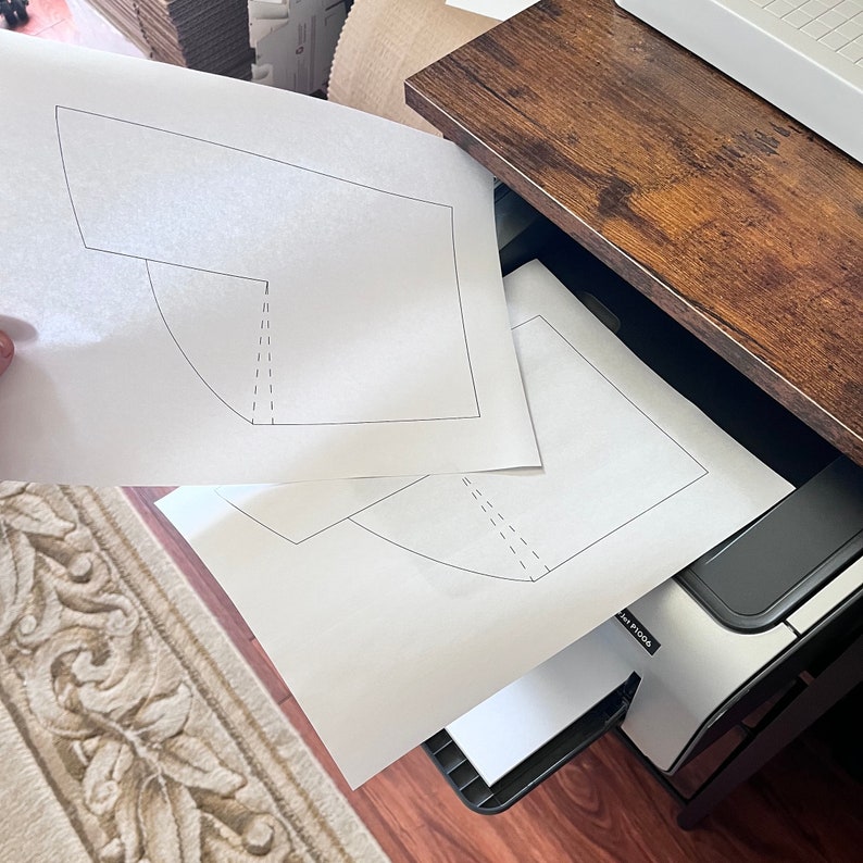 May include: Two white sheets of paper with a simple geometric design printed on them are being fed into a printer. The printer is black and silver with the text "HP PHOTO" visible on the front.