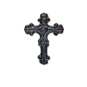 May include: A ceramic cross ornament featuring a dark brown and deep blue glazed finish. The cross has an ornate, scrolled shape with rounded edges and a small circular hole at the top for hanging. The surface shows a glossy, variegated texture.