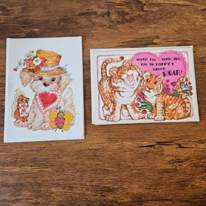 May include: Two vintage Valentine's Day cards. One card features a puppy wearing a hat and holding a heart. The other card has two tigers with the text "When I'm with you, I'm so happy I could ROAR!"
