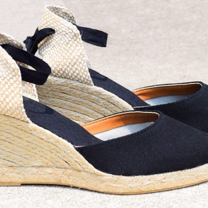Peut inclure: Une paire de sandales compens&eacute;es en espadrilles noires avec une semelle en corde et des lacets noirs.