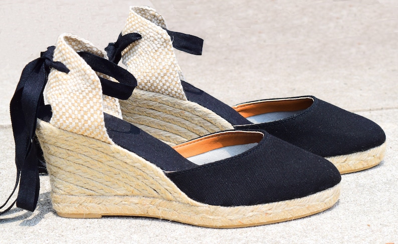 Peut inclure: Une paire de sandales compens&eacute;es en espadrilles noires avec une semelle en corde et des lacets noirs.
