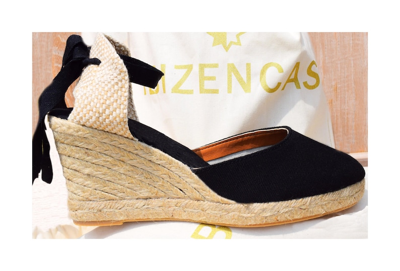 Peut inclure: Sandales compens&eacute;es en espadrille noires avec une plateforme en jute et un lacet noir. Les sandales sont sur une surface blanche avec le texte "Bizencas" visible.