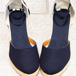 Peut inclure: Une paire d'espadrilles compens&eacute;es en toile noire avec une semelle en jute beige et une bride de cheville noire.