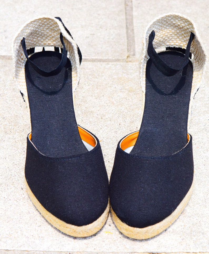 Peut inclure: Une paire d'espadrilles compens&eacute;es en toile noire avec une semelle en jute beige et une bride de cheville noire.
