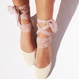May include: A pair of cream-colored canvas espadrilles with pink lace ties. The laces are tied around the ankles and create a bow at the top of the foot.