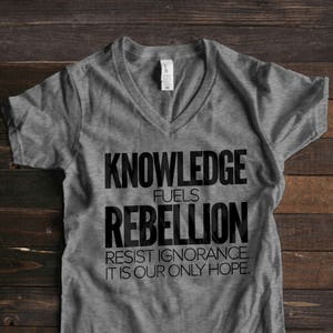 Puede incluir: Camiseta gris de cuello en V con texto negro que dice "Knowledge fuels rebellion. Resist ignorance. It is our only hope."