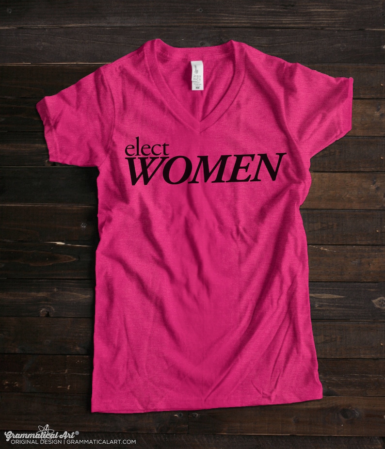 May include: Pink V-neck t-shirt with the text "elect WOMEN" printed in black.