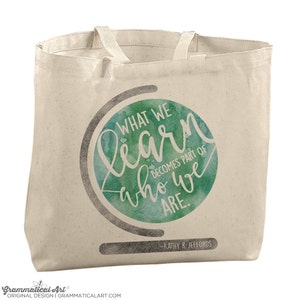 May include: A white canvas tote bag with a green watercolor globe design. The globe has the text "WHAT WE learn who we ARE. BECOMES PART OF" and "KATHY R. JEFFORDS" at the bottom.