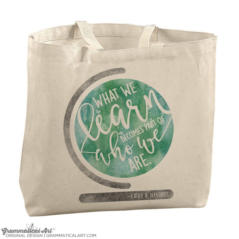 May include: A white canvas tote bag with a green watercolor globe design. The globe has the text "WHAT WE learn who we ARE. BECOMES PART OF" and "KATHY R. JEFFORDS" at the bottom.