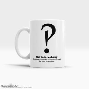 Puede incluir: Taza de cerámica blanca con un signo de interrogación y un signo de exclamación negros combinados en un solo símbolo. El texto "the interrobang" está impreso debajo del símbolo, junto con el texto "the only appropriate punctuation mark for your frustration".
