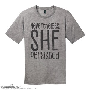 May include: A heather grey t-shirt with the text "Nevertheless, SHE persisted." printed in black.