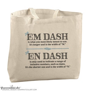 Può includere: Una borsa di tela beige con un design grafico in bianco e nero che spiega la differenza tra un trattino lungo e un trattino corto. Il testo dice "THE EM DASH is what you most likely meant to use. It's longer and is the width of "M." THE EN DASH is only used to indicate a range of inclusive numbers, such as dates. It's the shorter one and is the width of "N."