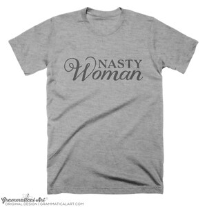 May include: A heather gray t-shirt with the text "Nasty Woman" in a cursive font.