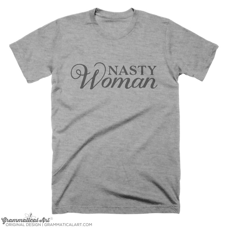 May include: A heather gray t-shirt with the text "Nasty Woman" in a cursive font.