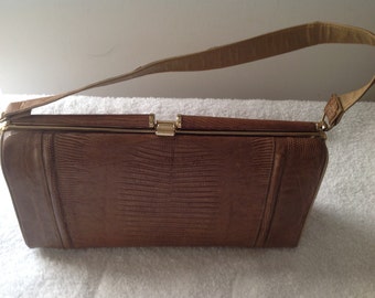 Könnte beinhalten: Eine braune Ledertasche mit einem goldenen Verschluss und einem langen Riemen. Die Tasche hat ein strukturiertes, geprägtes Muster.
