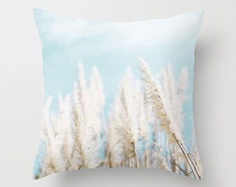May include: A throw pillow featuring a photograph of white pampas grass against a light blue sky.