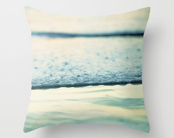 May include: A close-up of a wave breaking on a sandy beach. The water is a light blue and the sand is a light yellow. The image is taken from a low angle, so the wave appears to be very large.