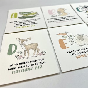 Op de afbeelding: Een set alfabetkaarten met elk een ander dier en een bijbelvers. De kaarten zijn wit met een lichtbruine achtergrond. De letters zijn in een kleurrijk lettertype. De dieren zijn ge&iuml;llustreerd in aquarelstijl. De verzen zijn in zwarte tekst gedrukt. De kaarten zijn voor kinderen en een geweldige manier om hen de bijbel te leren.