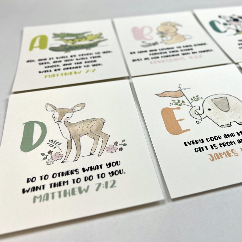 Op de afbeelding: Een set alfabetkaarten met elk een ander dier en een bijbelvers. De kaarten zijn wit met een lichtbruine achtergrond. De letters zijn in een kleurrijk lettertype. De dieren zijn ge&iuml;llustreerd in aquarelstijl. De verzen zijn in zwarte tekst gedrukt. De kaarten zijn voor kinderen en een geweldige manier om hen de bijbel te leren.